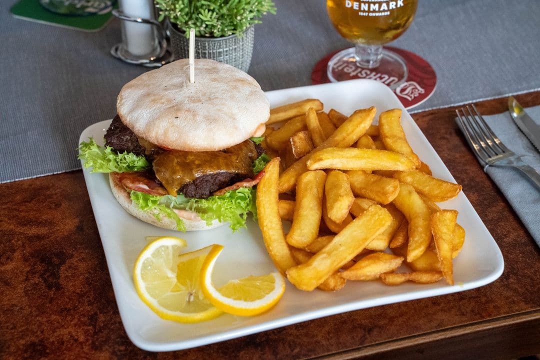 Burger im Brötchen mit dicken Pommes, daneben ein Glas Bier