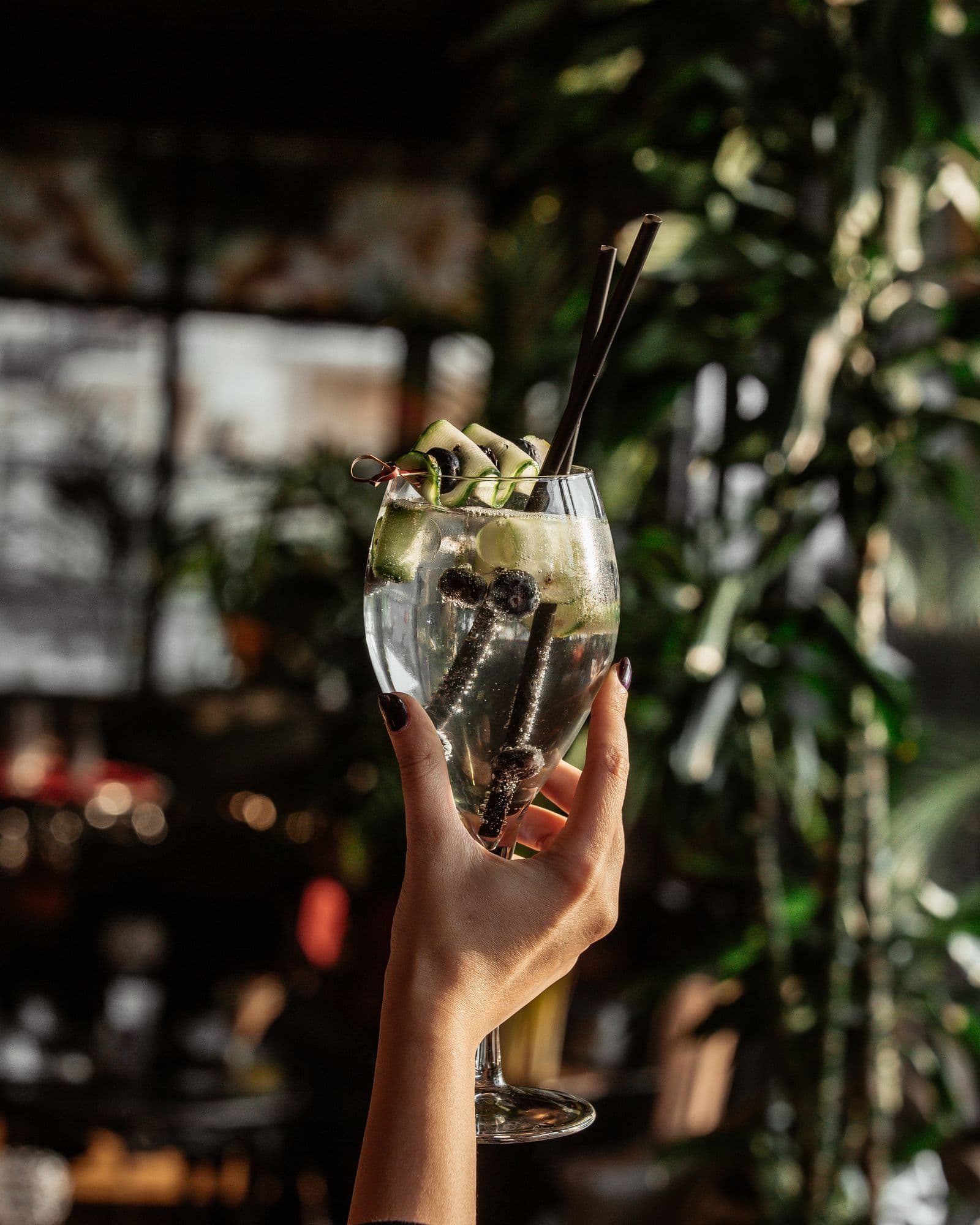 Hochgehaltener Gin Tonic mit Gurke und Blaubeeren vor der Bar im Restaurant Sulsdorf