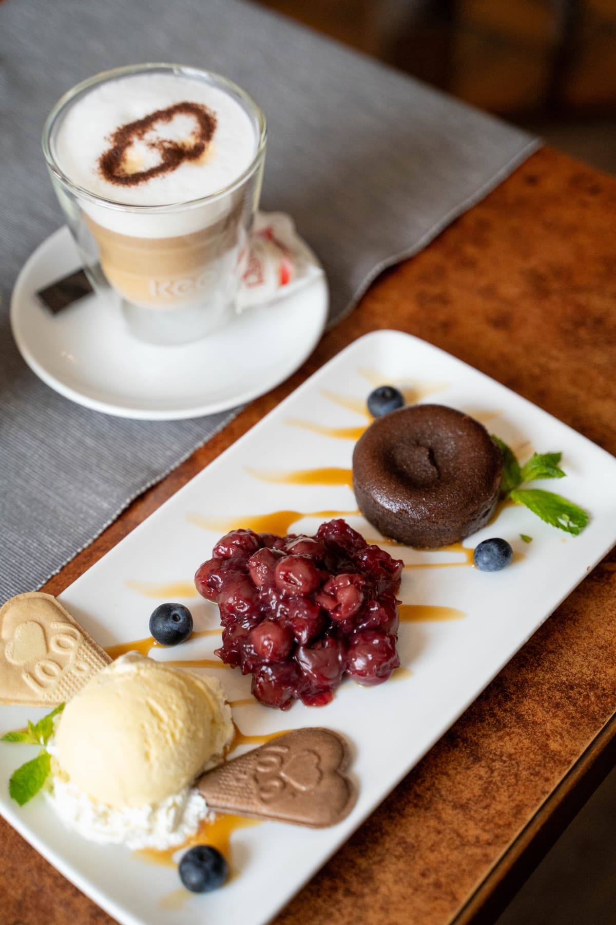 Schokoladenküchlein mit Kirschen, Vanilleeis und Latte Macchiato auf dem Tisch