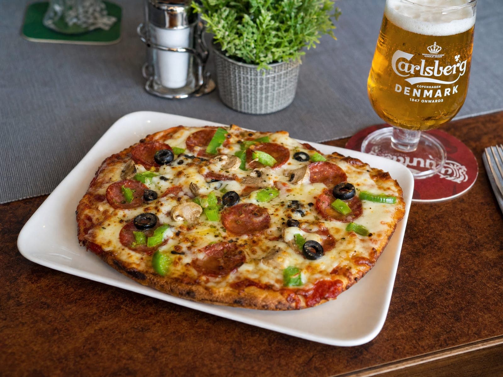 Pizza mit Salami, Champignons, Oliven und Paprika, daneben ein frisch gezapftes Bier