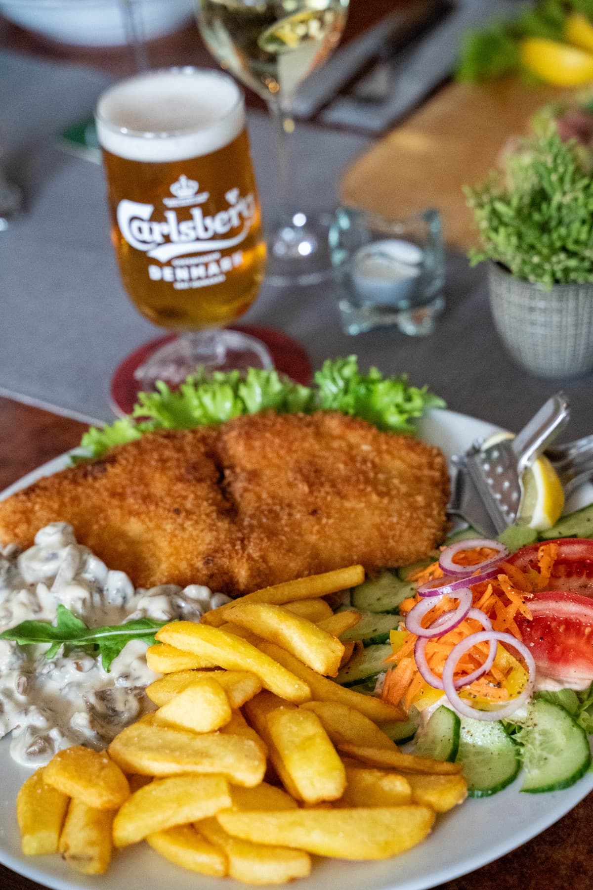 Paniertes Schnitzel mit Champignonrahm, Pommes und Salat auf dem Tisch im Gastraum