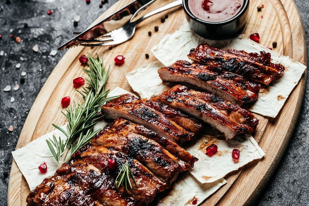 Glasierte Spareribs auf einem Holzbrett, dazu Barbecuesoße